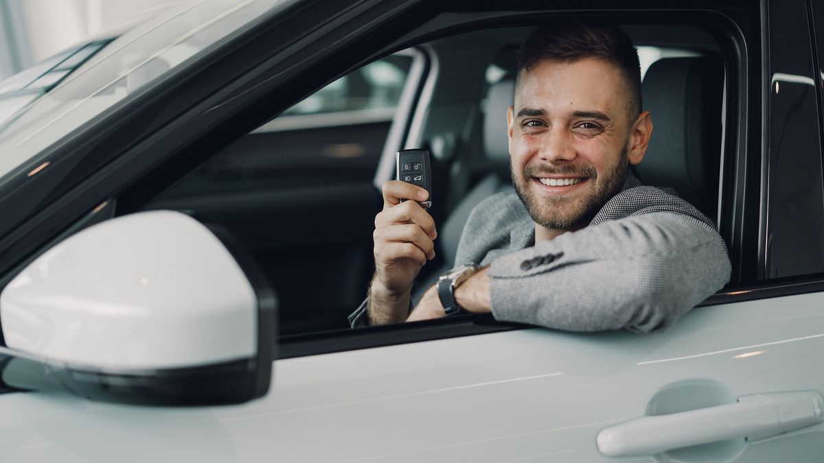 Besišypsantis vyras automobilyje laiko naujo automobilio raktelius